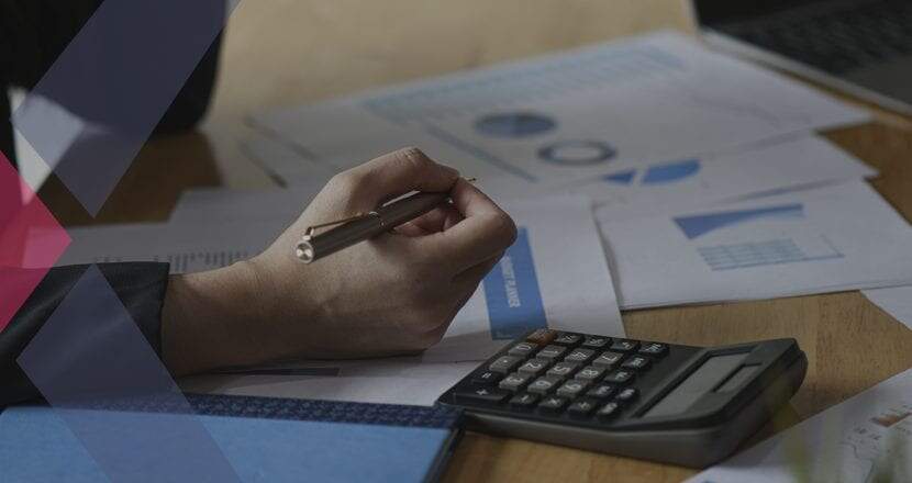 Uma mão humana segurando uma caneta, analisando relatórios financeiros ao lado de uma calculadora
