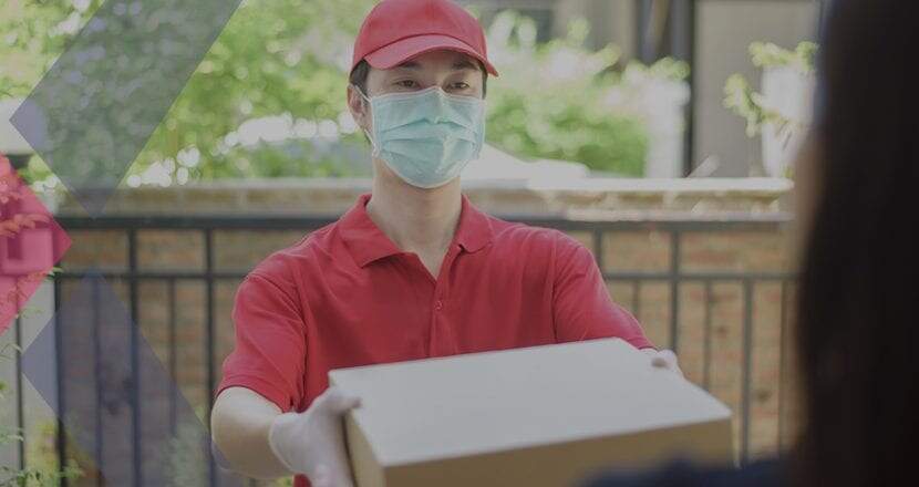 Rapaz vestindo blusa pólo vermelha e usando boné também vermelho fazendo entrega de uma encomenda dentro de uma caixa de papelão feita por delivery
