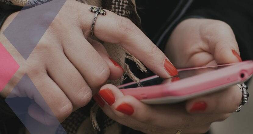 Mãos de uma mulher com unhas pintadas de vermelho realizando pagamento via Pix em seu celular rosa