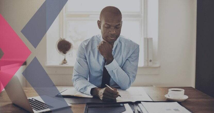 Homem negro vestindo camisa social azul-clara e uma gravata azul marinho, sentado na sua mesa de trabalho, analisando a contabilidade dos clientes em um relatório de papel.
